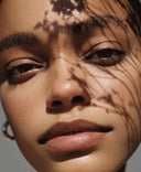 Close-up of a woman’s face with natural skin texture and soft shadows of flowers, symbolizing Audrose®’s balance of clinically active results with calm, gentle delivery for sensitive skin.