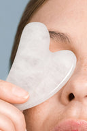 Close-up of a woman using a white gua sha stone on her face, demonstrating modern skincare tools that support hydration, calming, and protection when paired with Audrose® formulas.